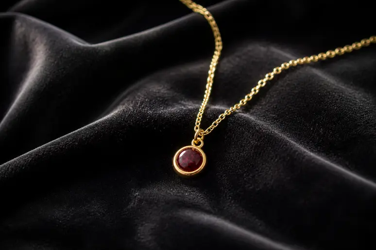 Pendentif délicat en or avec une pierre de porphyre rouge profond, rappelant la beauté et la durabilité d'une union de 33 ans.