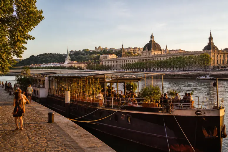 La Péniche La Marquise amarrée sur le Rhône à Lyon, illuminée par le soleil couchant avec l'Hôtel-Dieu en arrière-plan.