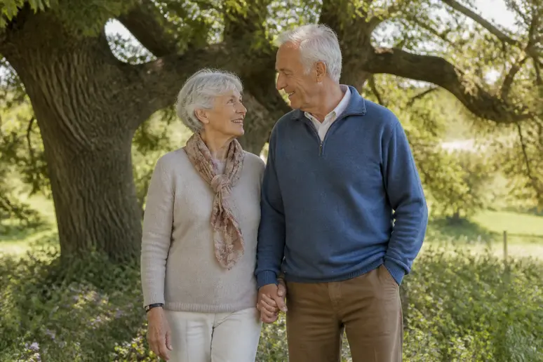 Un couple âgé de noces de chêne se tient la main dans un jardin, symbolisant 80 ans de mariage et d'amour durable.