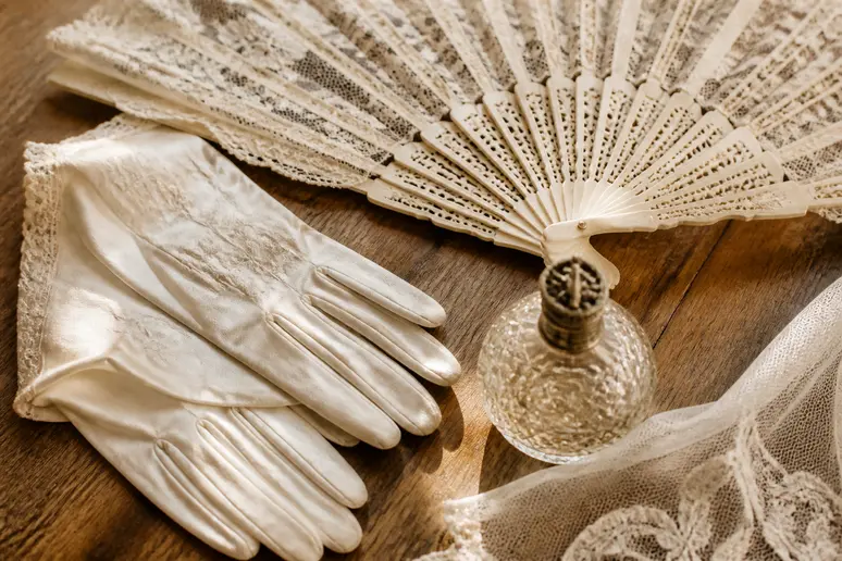 Accessoires de mariage vintage sur une table en bois : éventail en dentelle, gants élégants et flacon de parfum ancien.