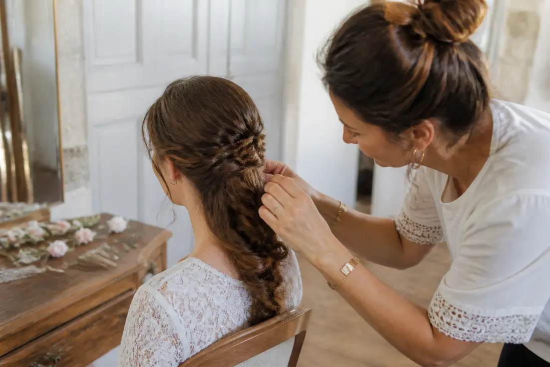 Une mariée aux longs cheveux bouclés reçoit une coiffure mariage cheveux longs tressée par un professionnel à Chartres.