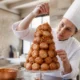 Un pâtissier assemble un croquembouche traditionnel avec du caramel dans une cuisine lumineuse