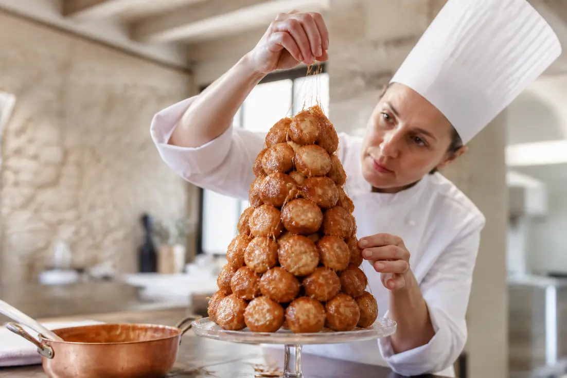 Un pâtissier assemble un croquembouche traditionnel avec du caramel dans une cuisine lumineuse