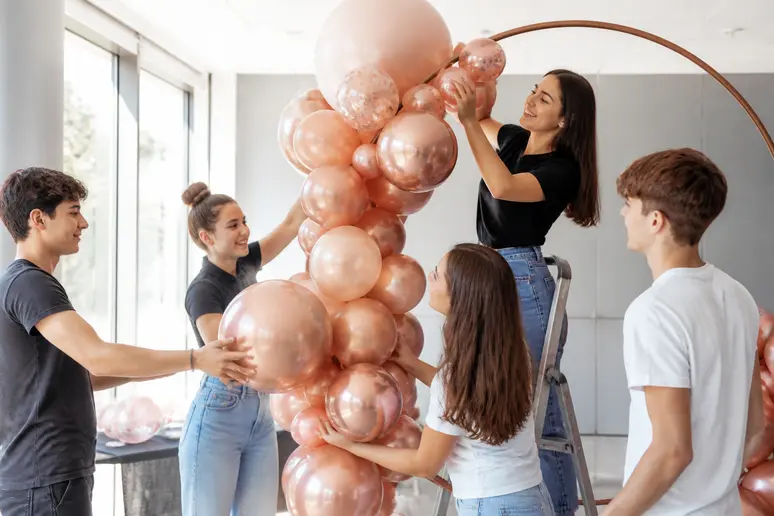 Jeunes Français créant une arche de ballons rose gold pour une deco anniversaire 18 ans réussie, ambiance festive et collaborative.