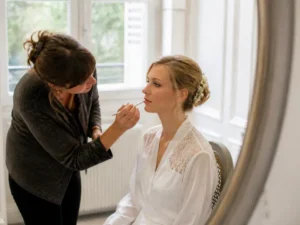 Une maquilleuse professionnelle prépare une mariée lumineuse avec un maquillage de mariage soigné dans une pièce lumineuse