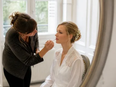 Une maquilleuse professionnelle prépare une mariée lumineuse avec un maquillage de mariage soigné dans une pièce lumineuse
