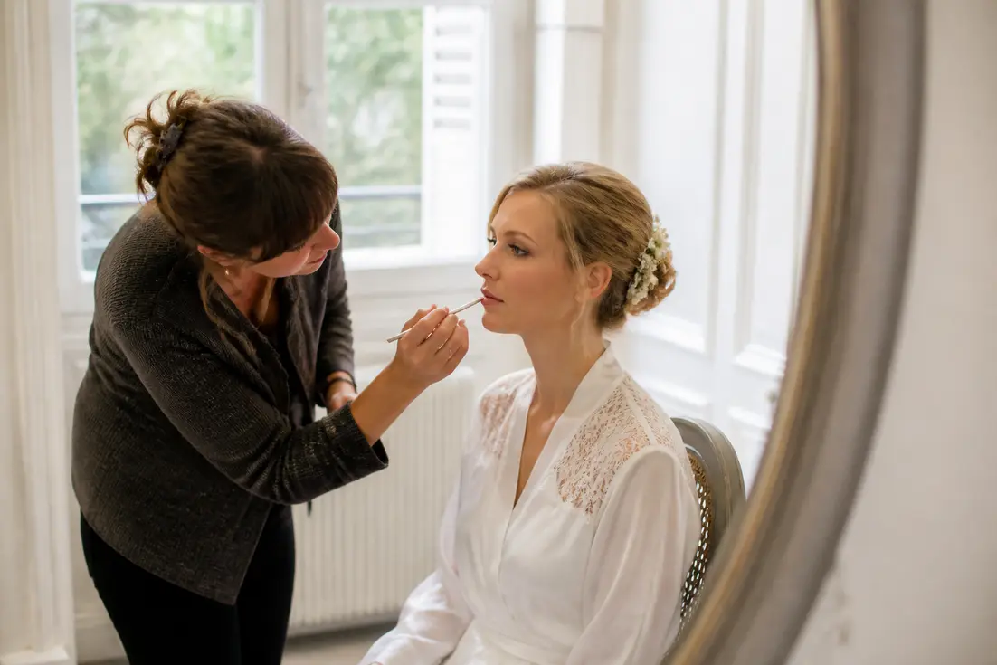 Une maquilleuse professionnelle prépare une mariée lumineuse avec un maquillage de mariage soigné dans une pièce lumineuse