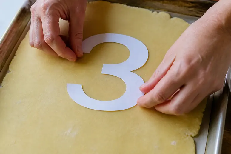 Découpe d'un number cake à l'aide d'un gabarit en papier posé sur la pâte sablée.