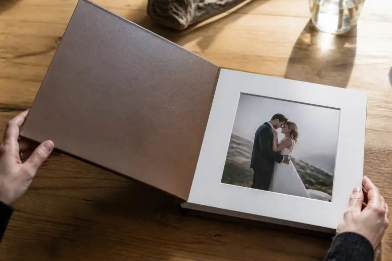 Mains ouvrant un livre photo personnalisé sur une table en bois pour consulter sa mise en page