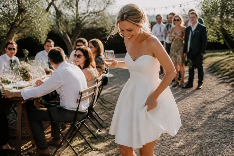 Jeune femme souriante portant une robe de mariée courte élégante lors d'une réception en extérieur