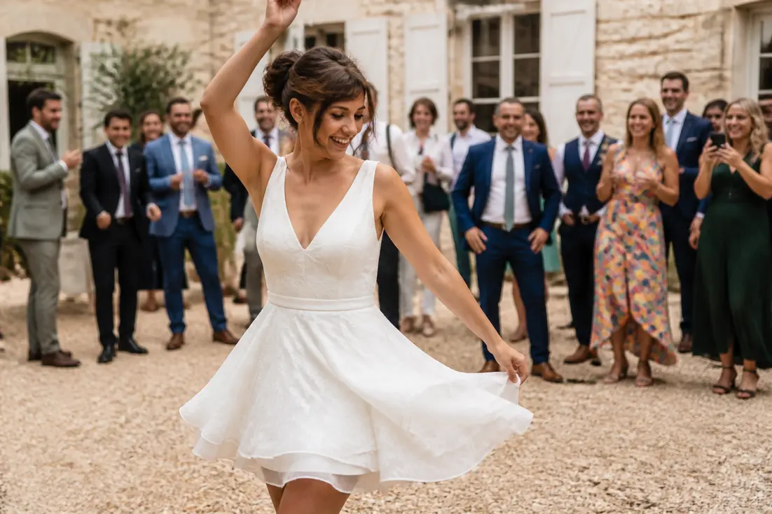 Jeune mariée souriante qui danse en portant une robe de mariée courte lors d'une réception de mariage.