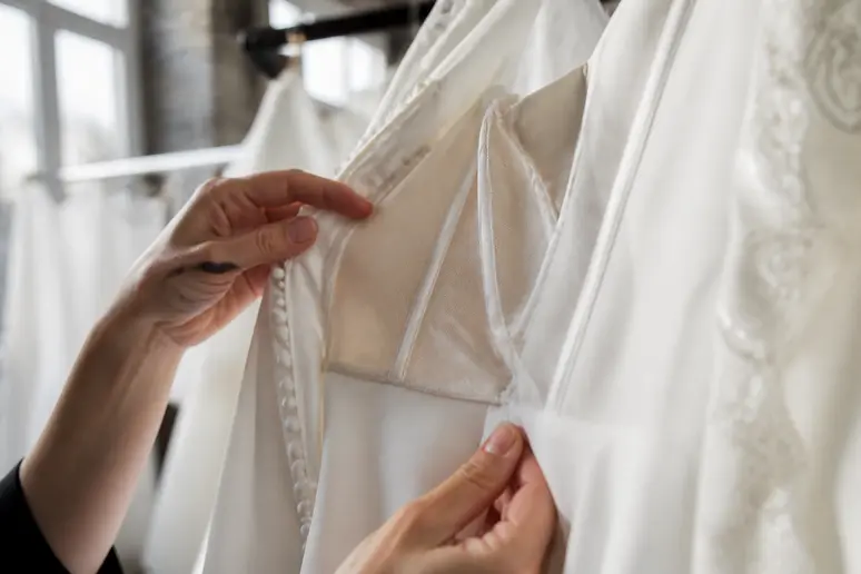 Mains examinant les coutures intérieures d'une robe de mariée pas cher suspendue dans un atelier lumineux