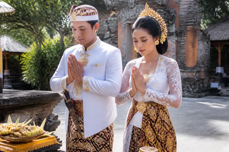 Couple balinais en tenue de mariage traditionnelle avec sarong lors d'une cérémonie paisible.