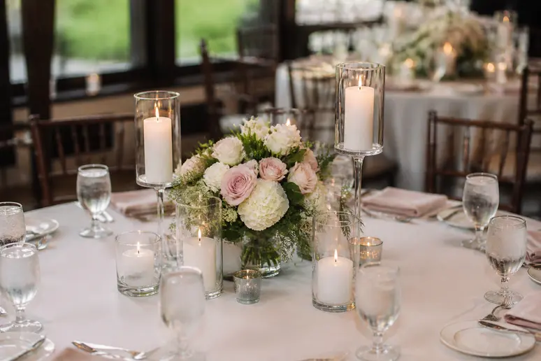 Plusieurs bougies disposées sur une table ronde de mariage aux côtés du centre de table floral