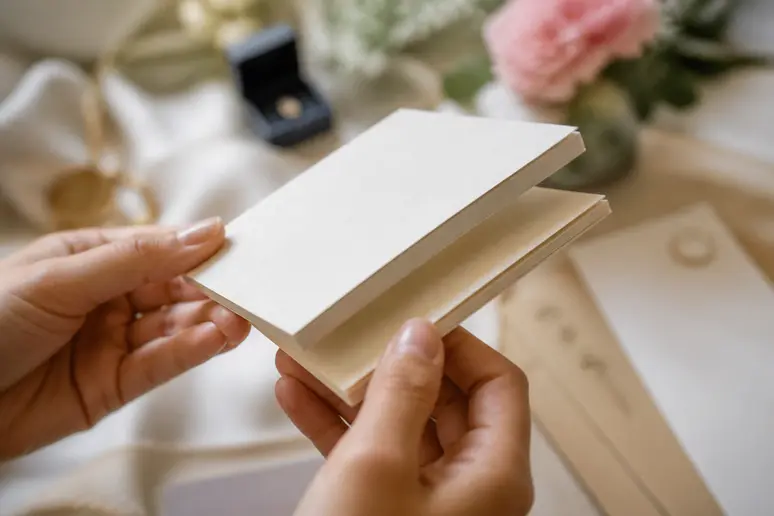 Mains tenant deux cartons d'invitation pour mariage afin de comparer leur épaisseur et leur rigidité.