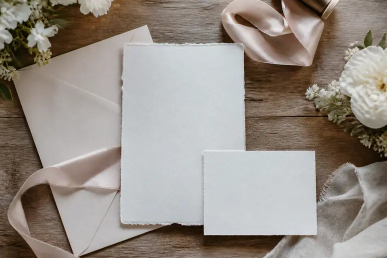 Ensemble d'une carte d'invitation pour mariage et de ses accessoires disposés sur une table en bois.