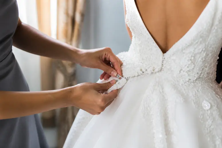 Mains fixant une traîne amovible à la taille d'une robe de mariée princesse volumineuse