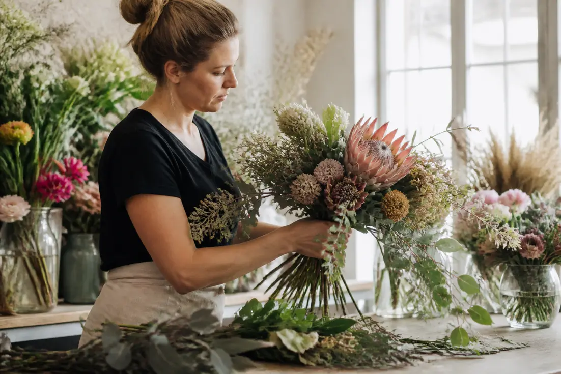 Artisan fleuriste préparant un robuste arrangement floral estival pour aider à choisir bouquet de mariée.