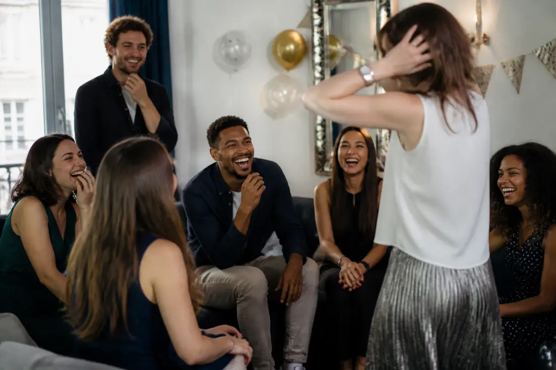 Amis riant ensemble lors d'une fête avec des jeux pour anniversaire adulte rigolo dans un salon chaleureux