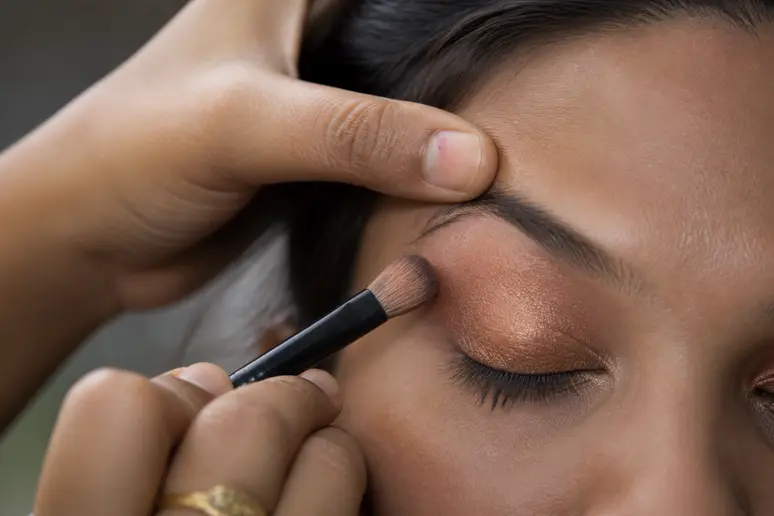 Application minutieuse d'un fard cuivré au pinceau sur la paupière pour un maquillage mariage yeux marrons
