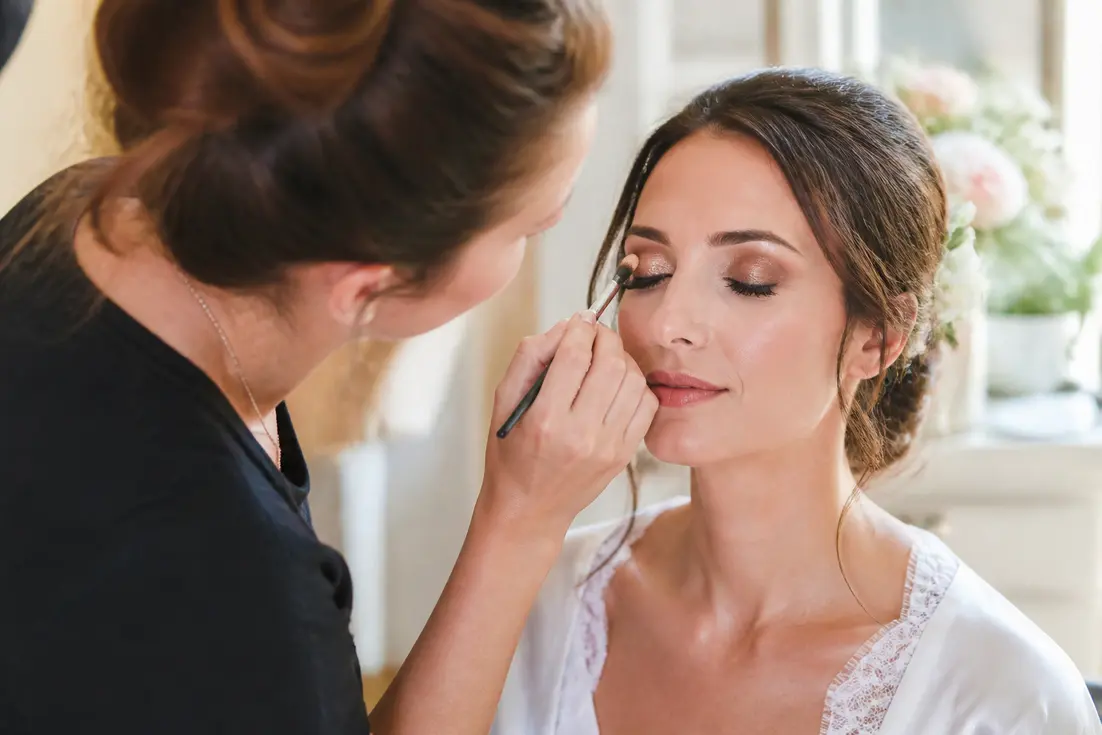 maquillage mariage yeux marrons appliqué avec délicatesse par une professionnelle dans un salon lumineux