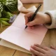 Une personne écrit un texte félicitation naissance fille sur une jolie carte rose pastel